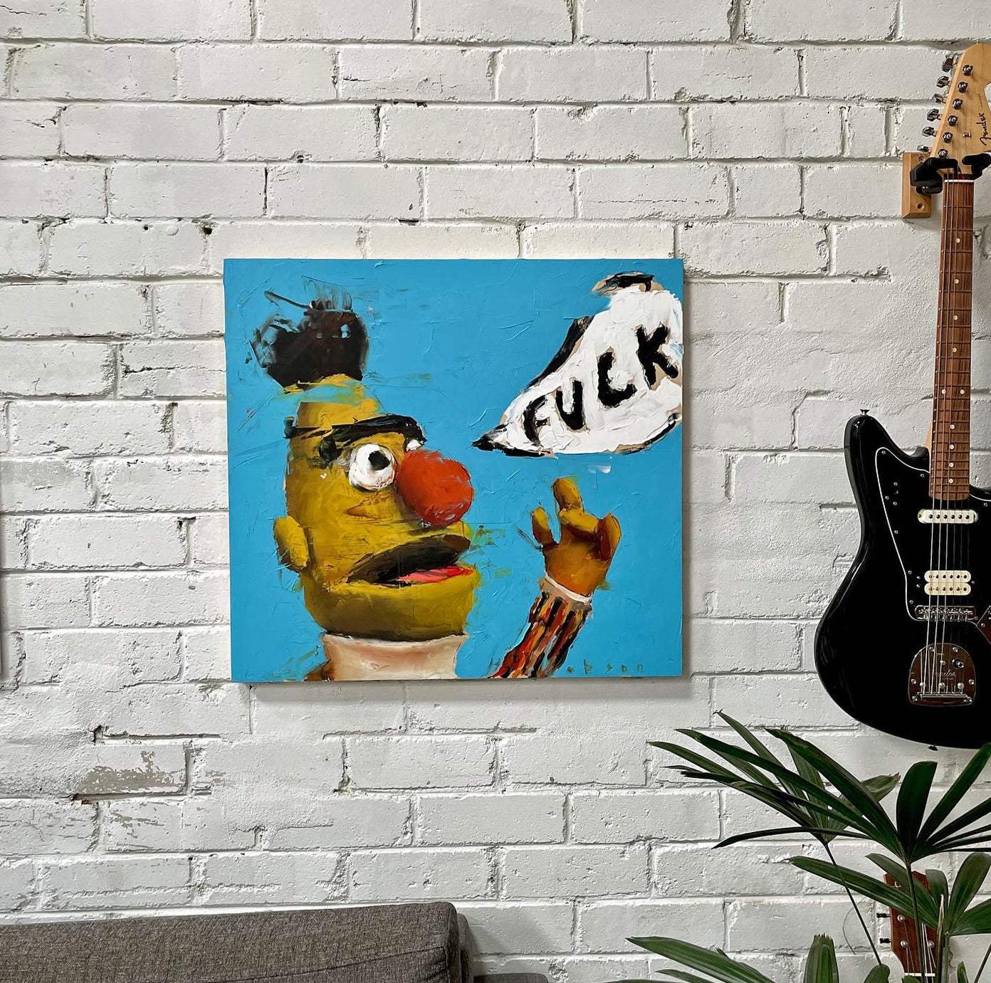 Painting of Bert from Sesame Street in a thick impasto style, shouting in a speech bubble against a bright blue background. The text in the bubble reads “F*CK.” Displayed on a white brick wall beside a black guitar — artwork by contemporary painter and muralist Robson.