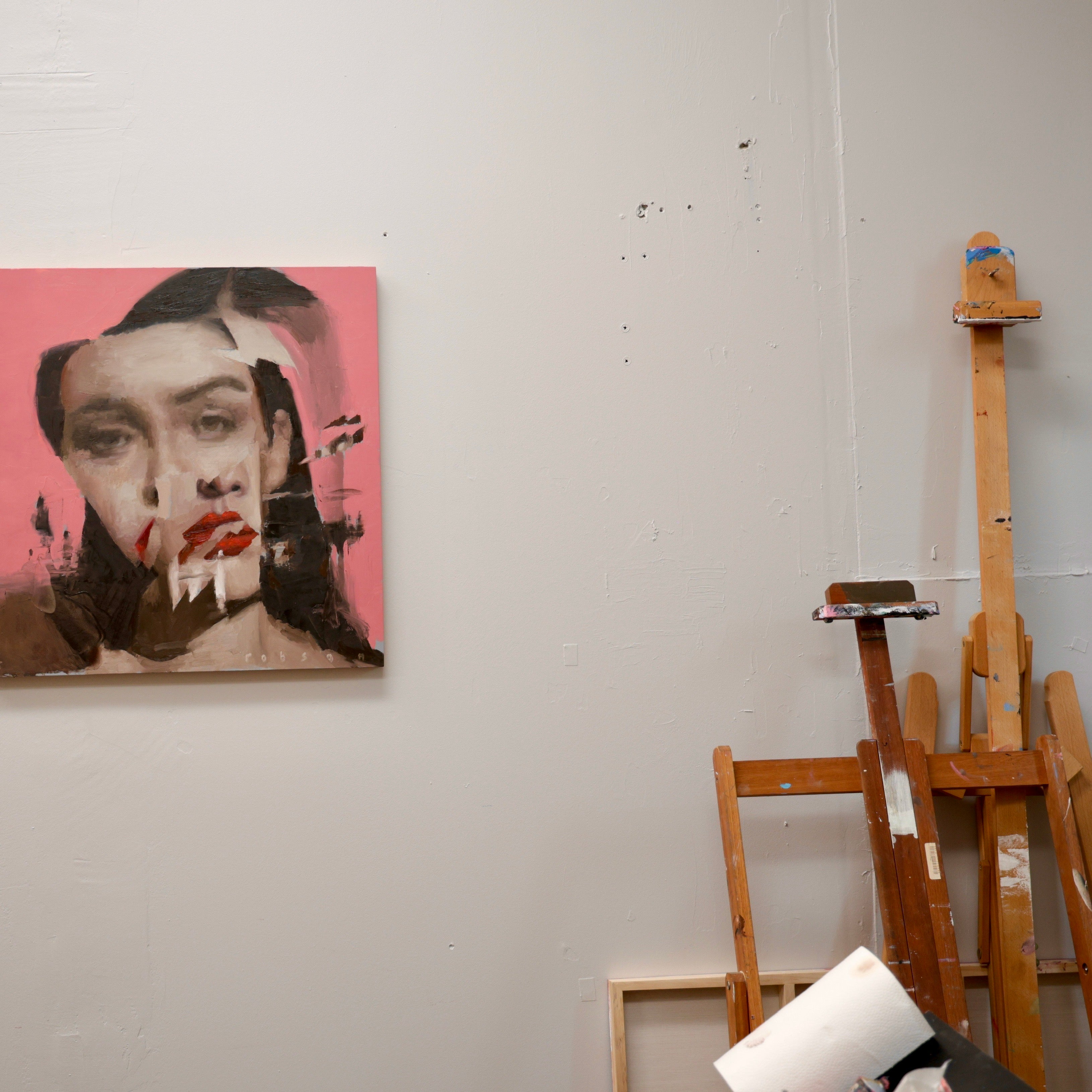 Art studio with a painting of a woman's face on a pink background and wooden easels.