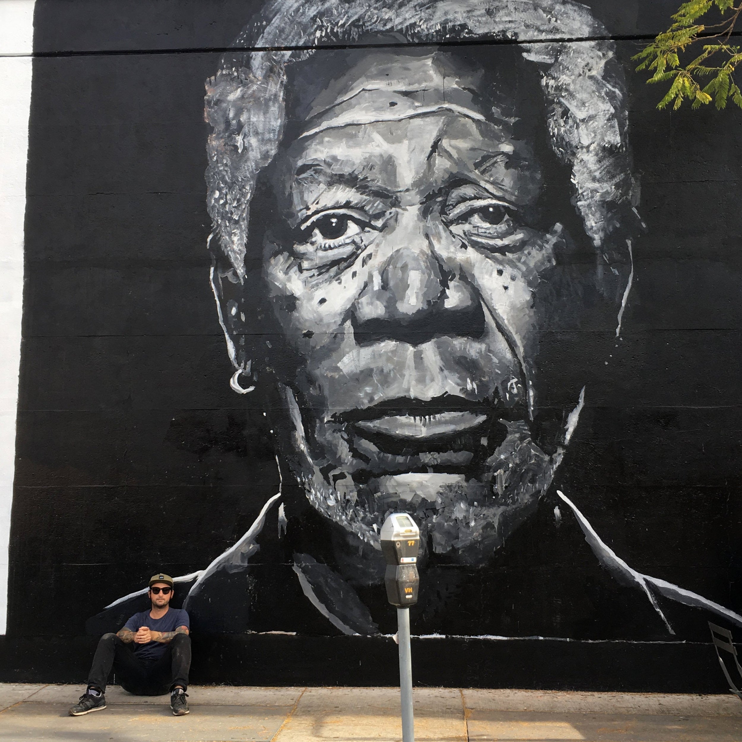 Robson artist sitting in front of a large mural of a man's face on a wall.